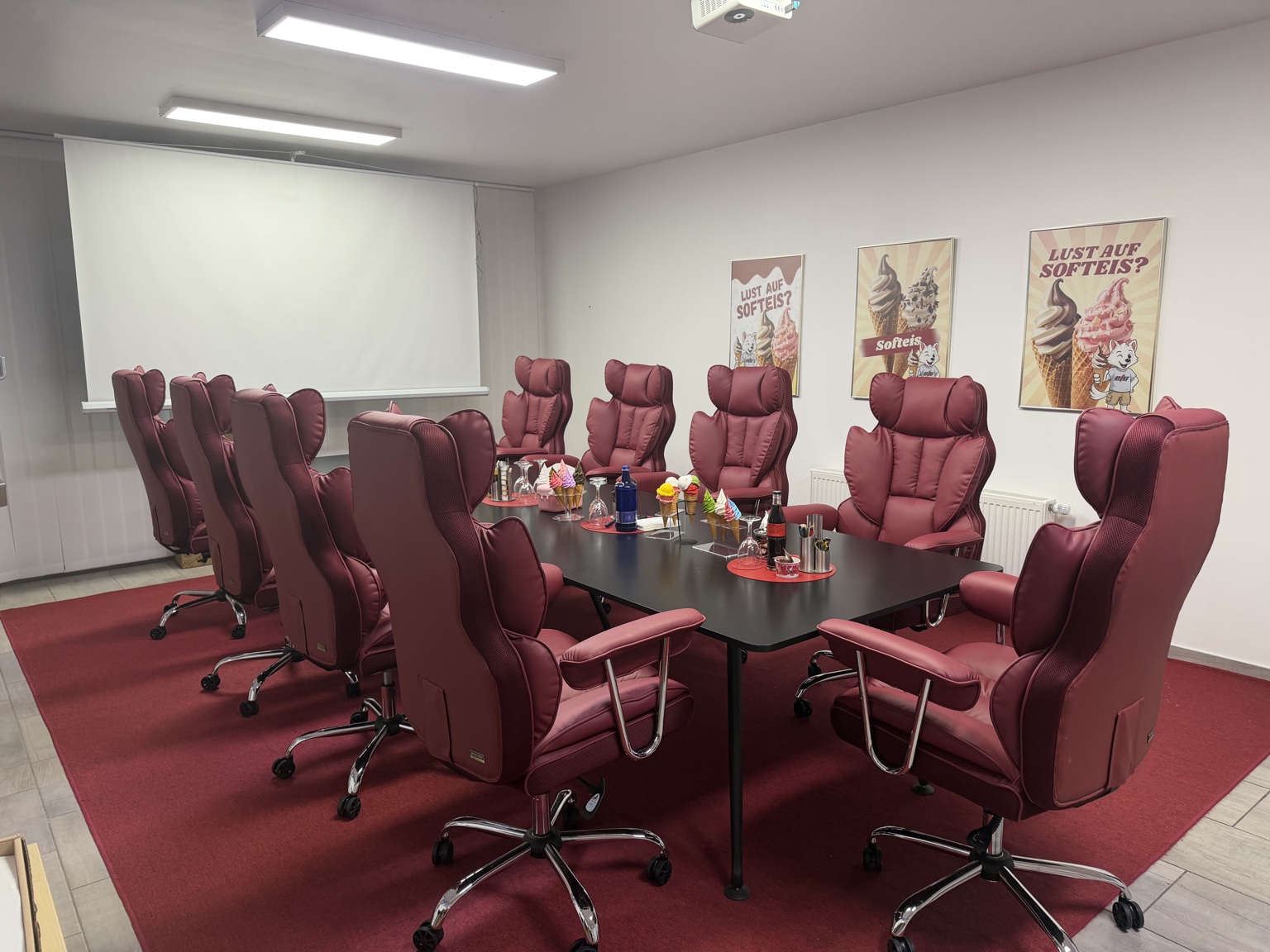 Besprechungs- und Schulungsraum des Eistechnikcenters mit bordeauxfarbenen Sesseln, großem Tisch, Leinwand und Beamer.