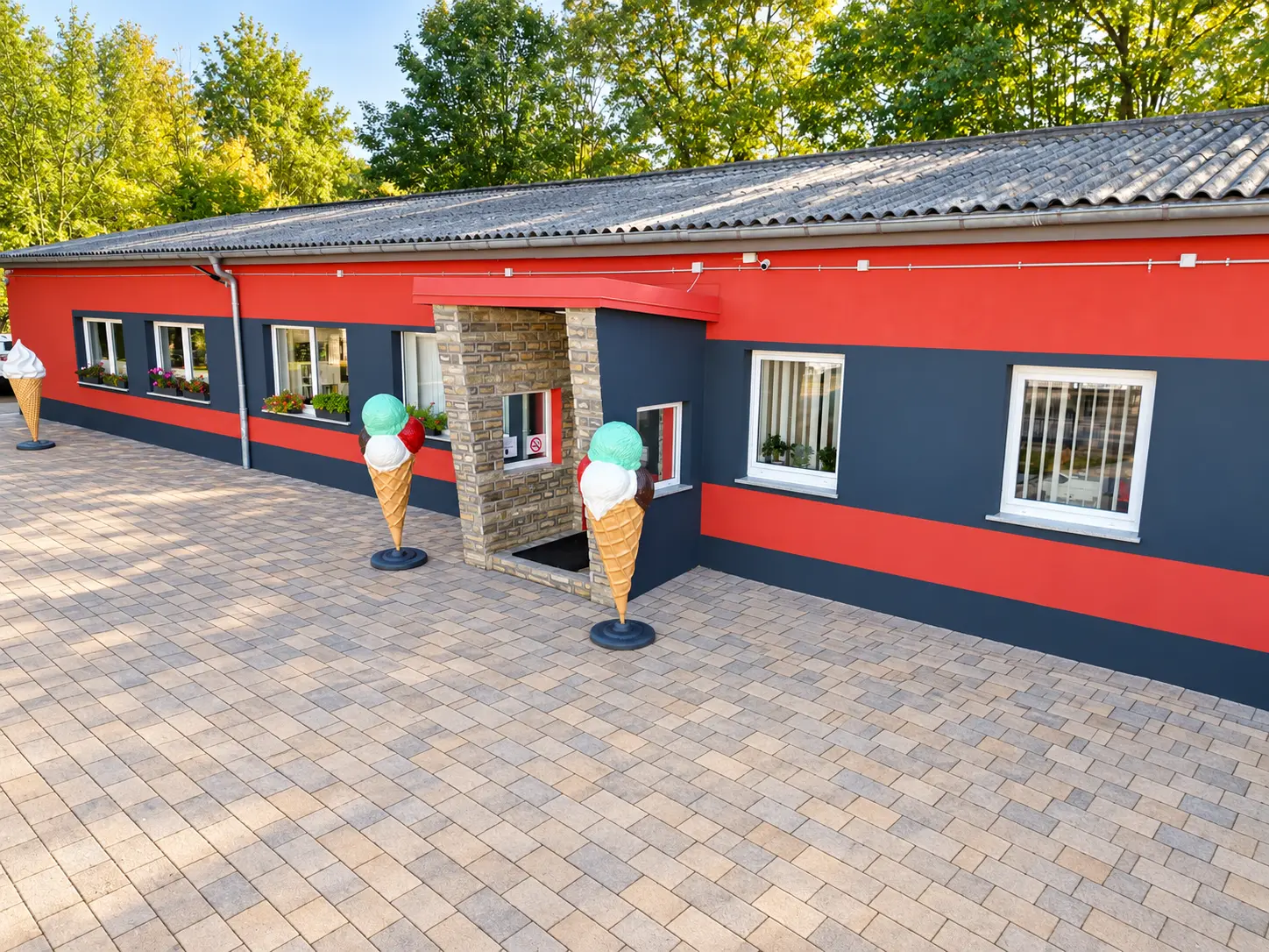 Eingang des Eistechnikcenters mit roter Fassade, dekorativen Eistüten und gepflastertem Vorplatz.