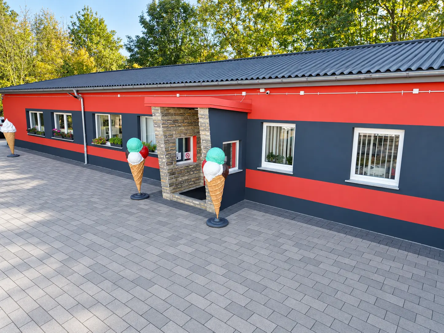 Bildbearbeitete Außenansicht des Eistechnikcenters in Luckenwalde mit roter Fassade, anthrazitfarbenem Dach und grauem Pflaster