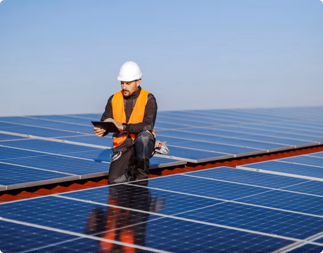 Solar technician in white hard hat and safety harness inspecting solar panels on a rooftop