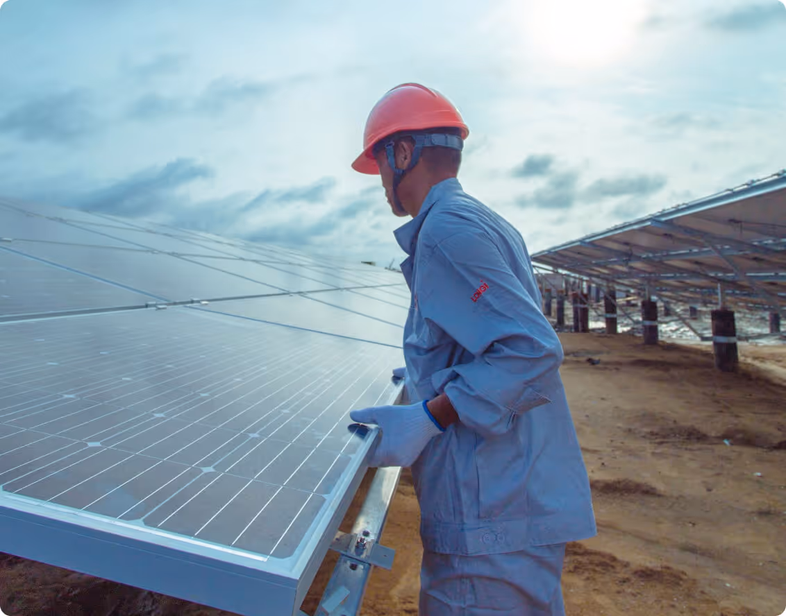 Solar worker in blue overalls and orange hard hat working alongside solar panels at a ground-mounted installation