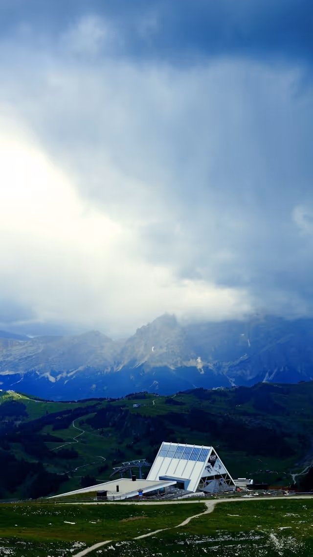 A solar-equipped structure in an alpine mountain setting under dramatic storm clouds, representing the long-term performance and durability of LONGi modules across challenging environments — from extreme heat and humidity to high-altitude conditions — backed by warranties of up to 30 years.