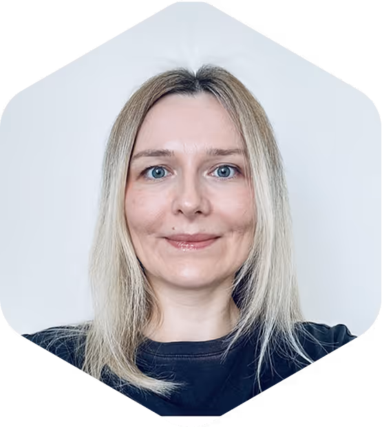 Portrait of a smiling woman with straight blonde hair and blue eyes wearing a dark top against a light background.
