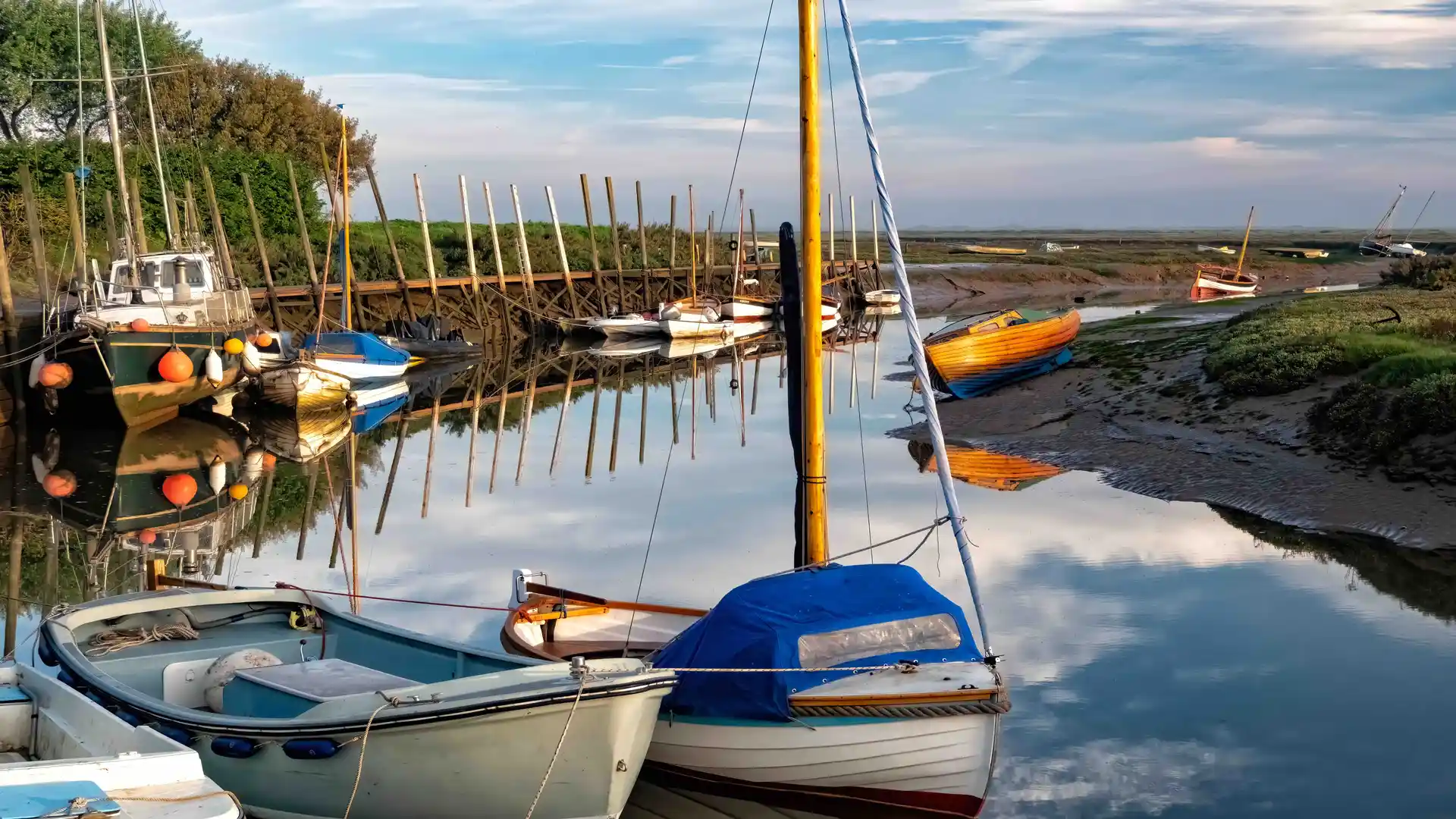 Moored boats in the quiet, reflective waters of Blakeney harbour at low tide.