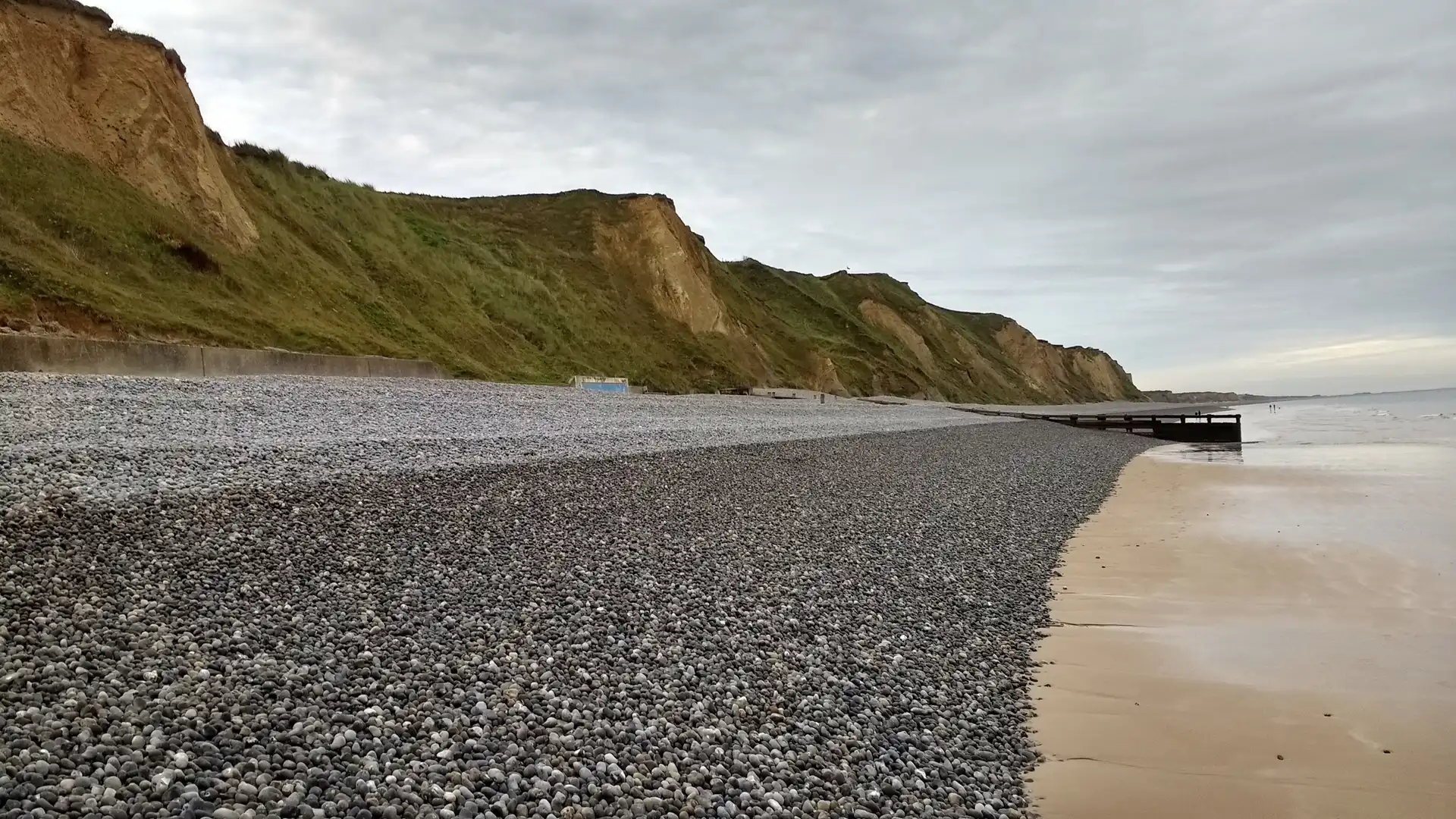 views alone a stone filled beach with rising hills over looking the sea, in Sheringham Norfolk.