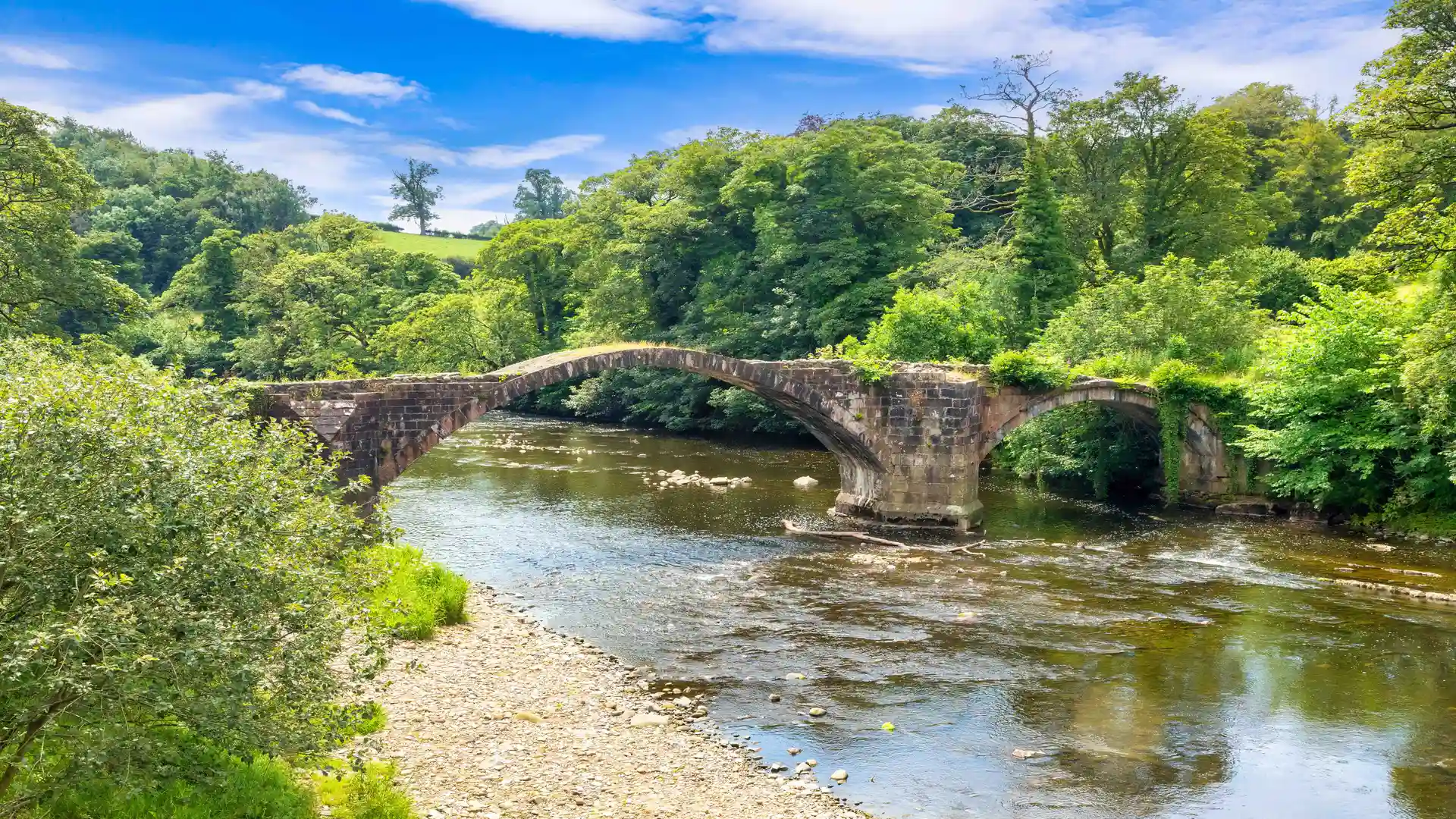 A stone built walkway bridge crosses the river in the forest of Bowland.
