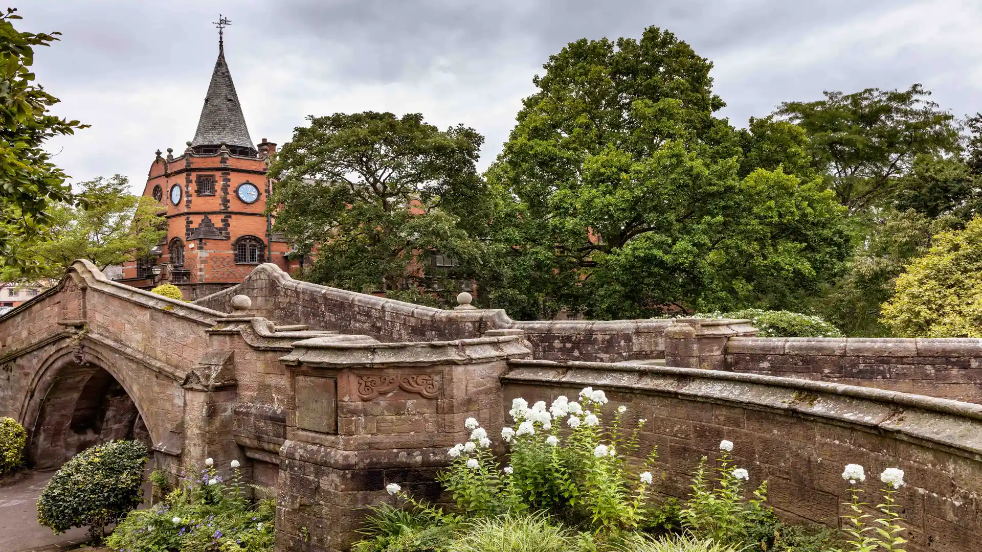 Brick and stone footbridge at the Dell in Port Sunlight Garden Village, Wirral, Merseyside — crossing a shaded stream amid landscaped gardens