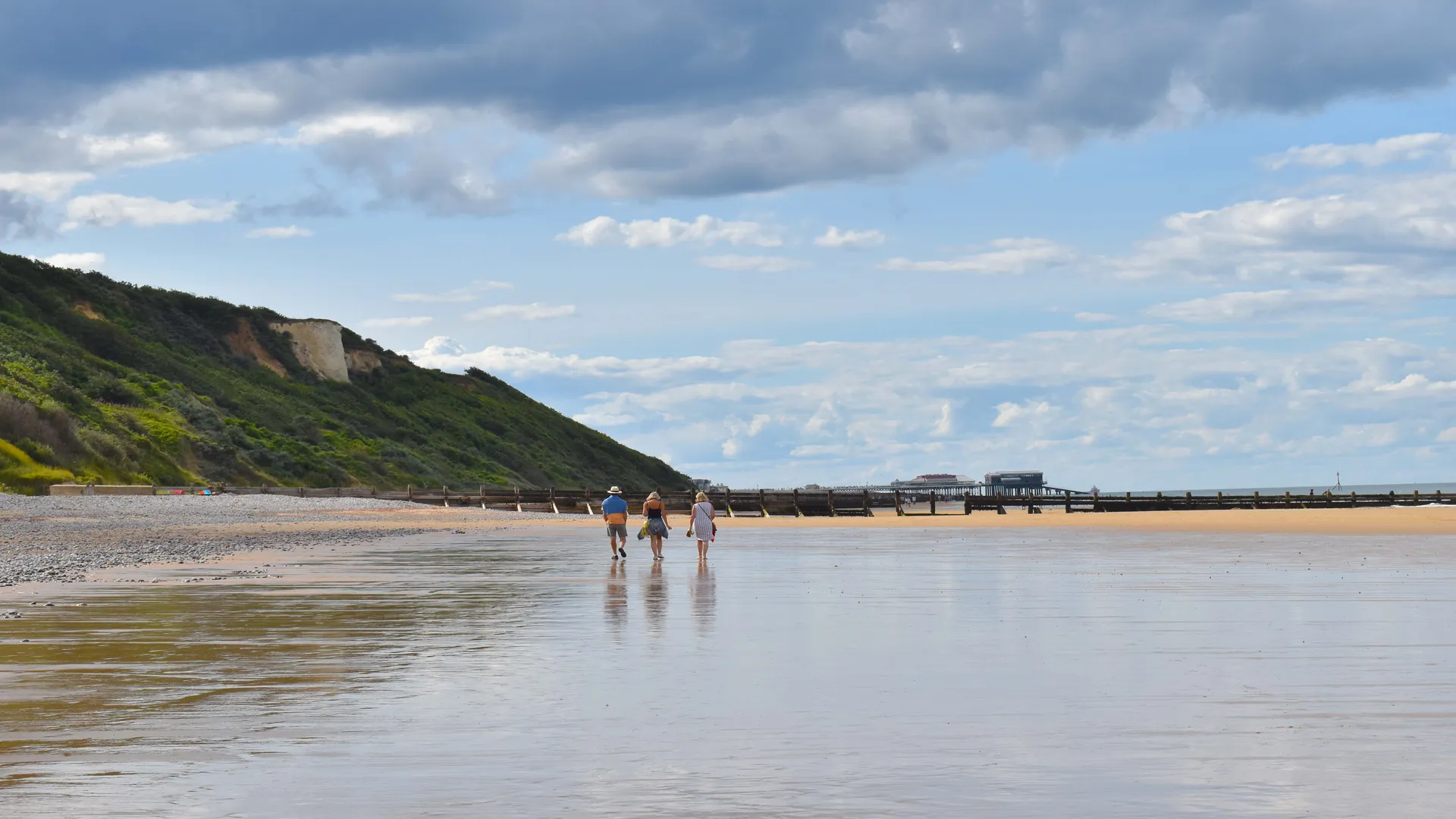 view along a shoreline on the Norfolk cost with sandy beach blue skies and beach trees.