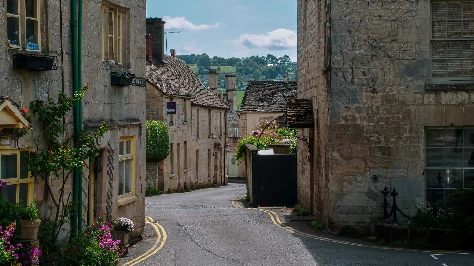 A street view of Painswick village on a sunny day with golden coloured old houses 