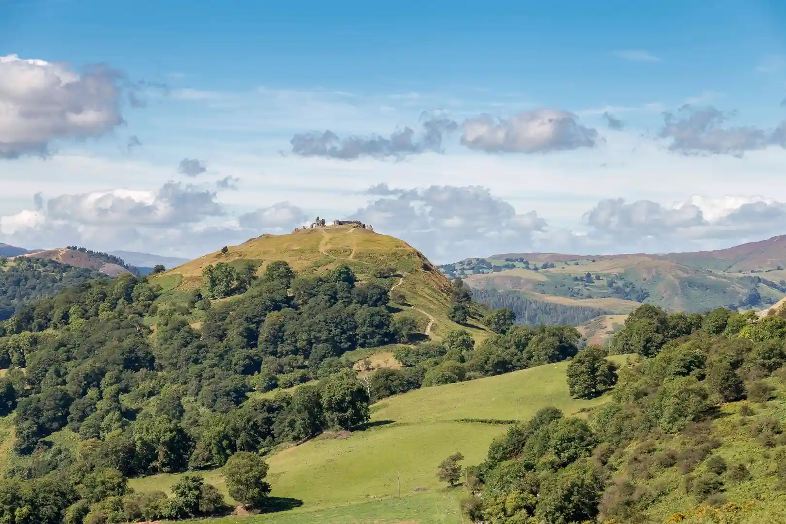 View of Castell Dinas Brân perched on a hilltop above the green valleys of Llangollen, with rolling hills and scattered clouds in the distance, Denbighshire, North Wales.