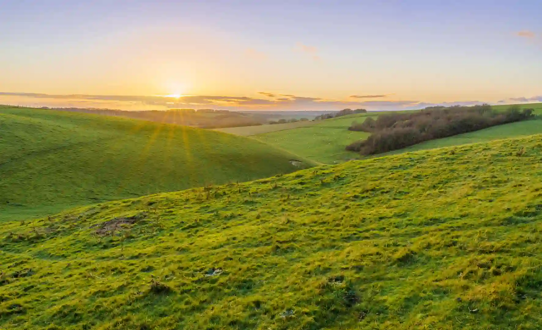 A golden sunset, low illuminated cloud on the horizon over a deep green grass valley, North Wessex Downs AONB