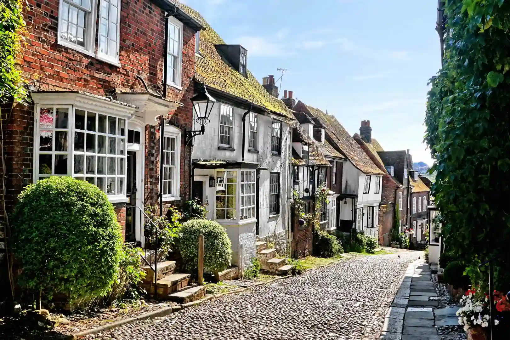 Cobbled Mermaid Street in Rye, East Sussex, lined with historic timbered and brick houses on a sunny day.