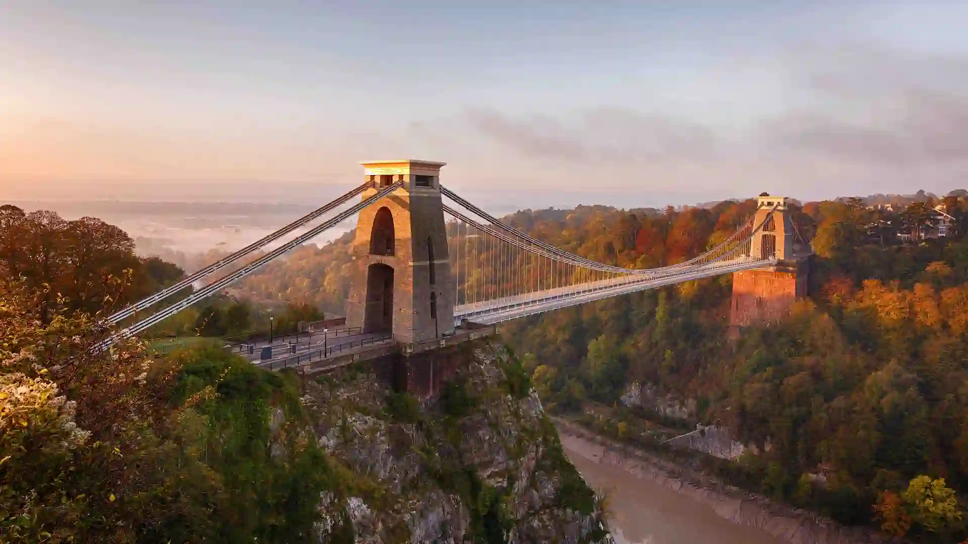Clifton Suspension Bridge spanning the Avon Gorge at sunrise, surrounded by autumn trees, Bristol, England.