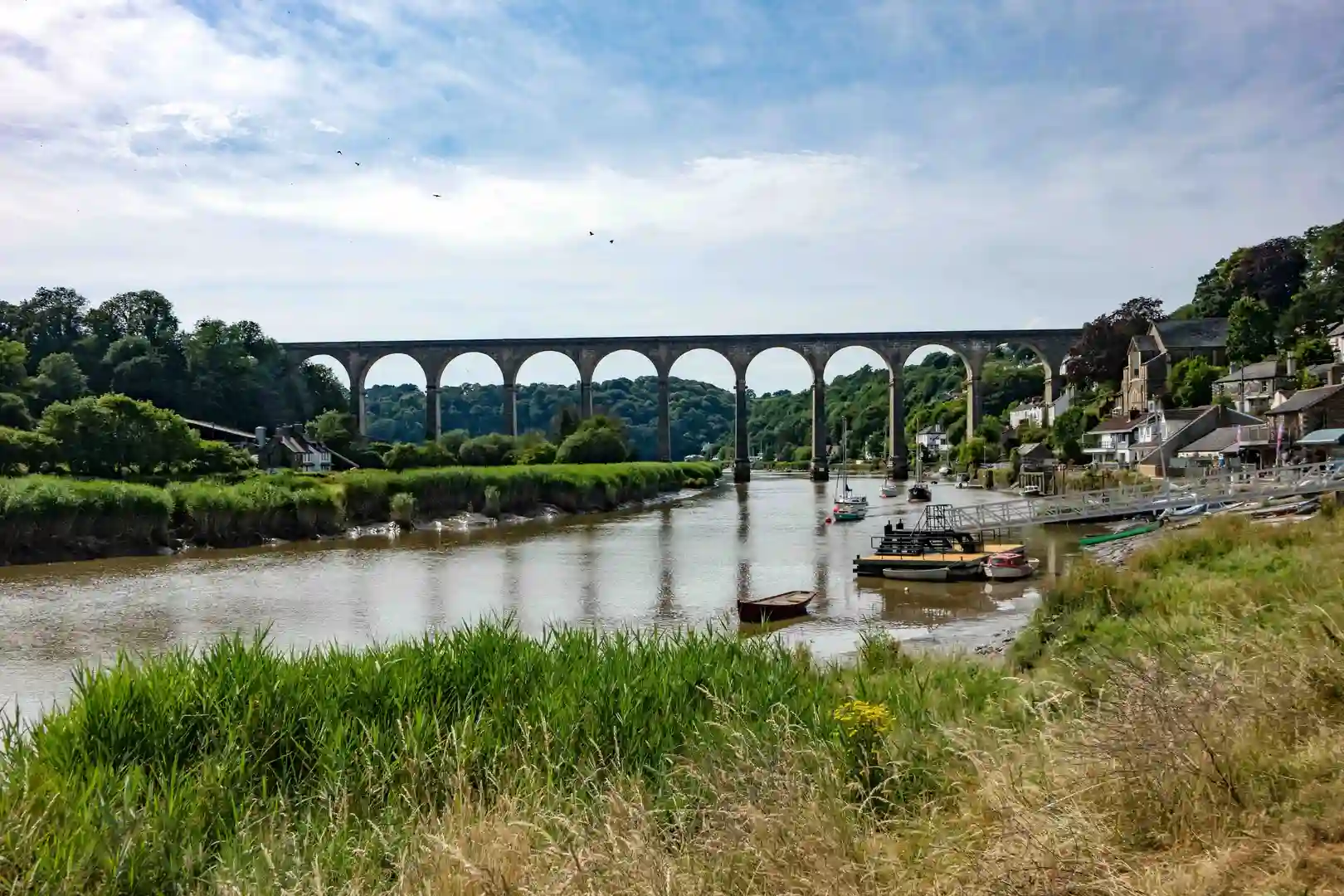 Calstock Viaduct crossing the River Tamar in the Tamar Valley National Landscape, with boats moored along the riverside and green woodland hills in the background.