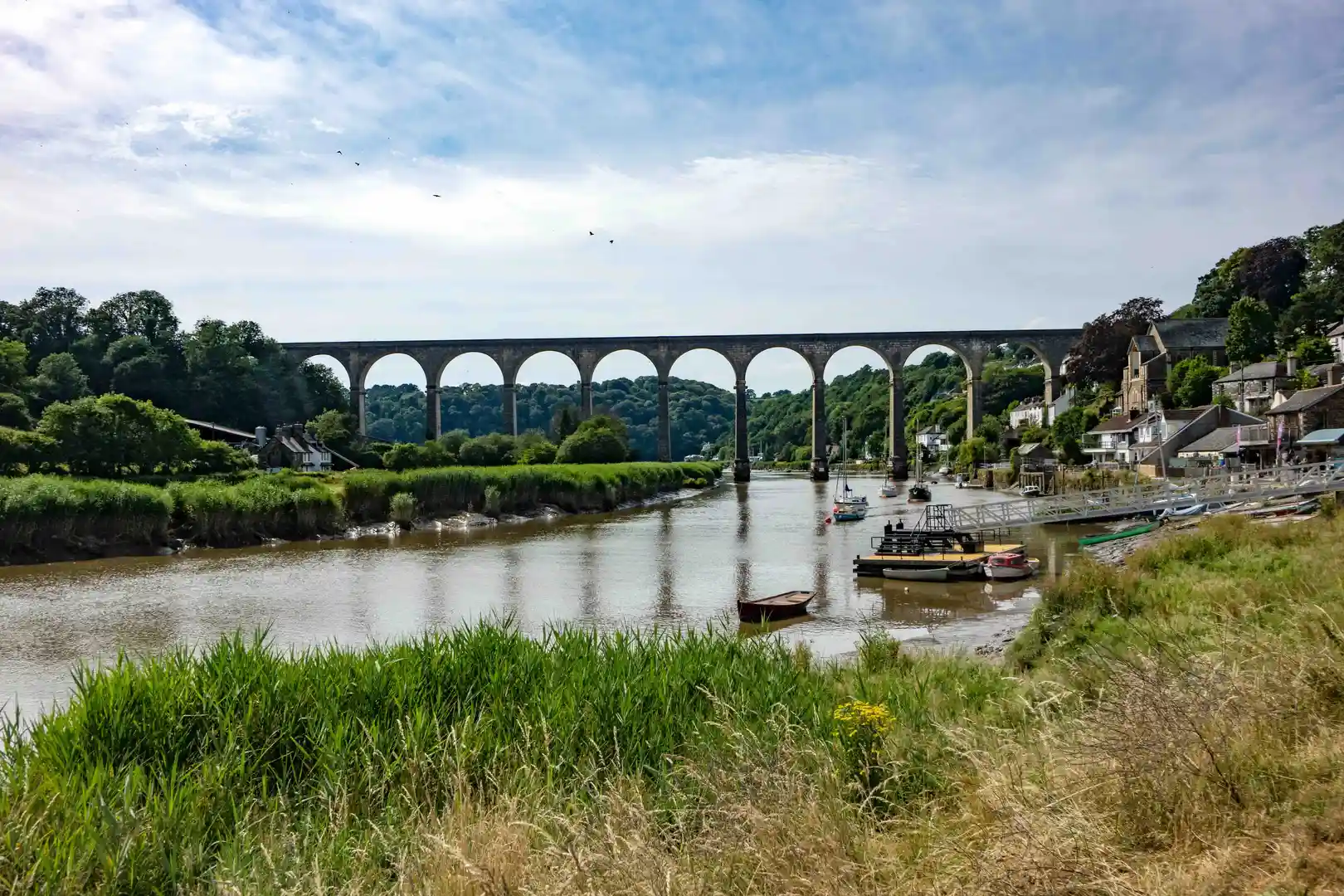 Calstock Viaduct crossing the River Tamar in the Tamar Valley National Landscape, with boats moored along the riverside and green woodland hills in the background.