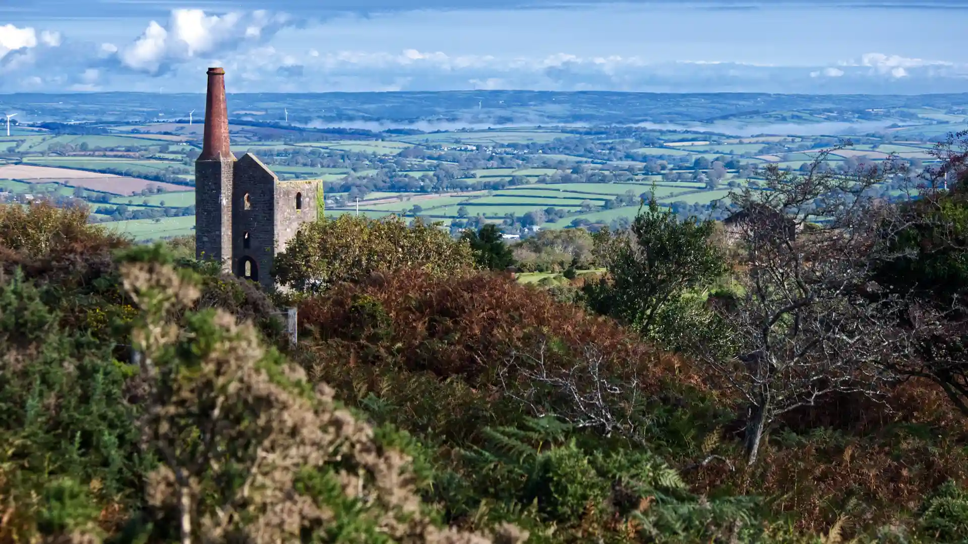Historic tin mine engine house on a hillside in the Cornwall and West Devon Mining Landscape, overlooking patchwork fields and countryside in South West England.