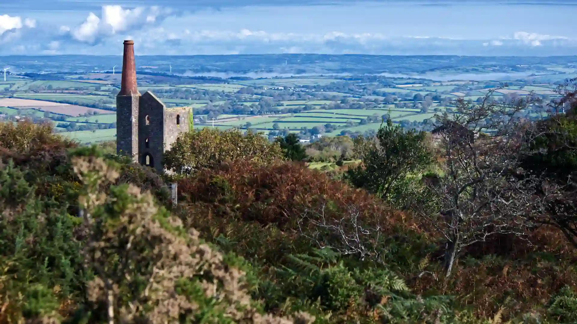 Historic tin mine engine house on a hillside in the Cornwall and West Devon Mining Landscape, overlooking patchwork fields and countryside in South West England.