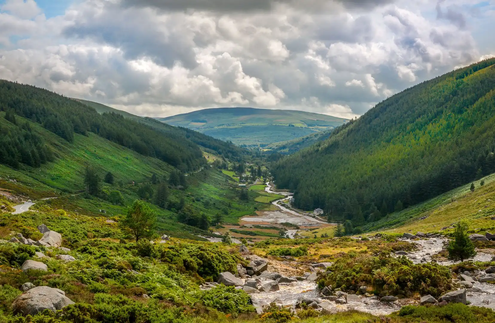 Scenic valley view in County Wicklow, Ireland, with forested hills, a winding river, and mountain backdrop in the Wicklow Mountains National Park