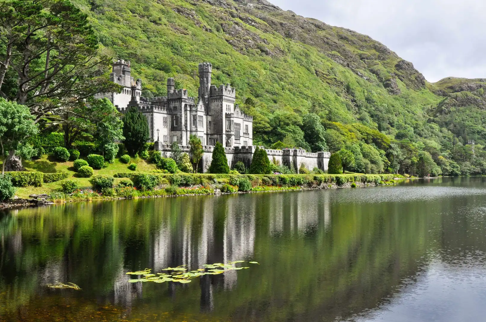 Kylemore Abbey reflected in the lake, surrounded by lush green hills in Connemara, County Galway, Ireland.