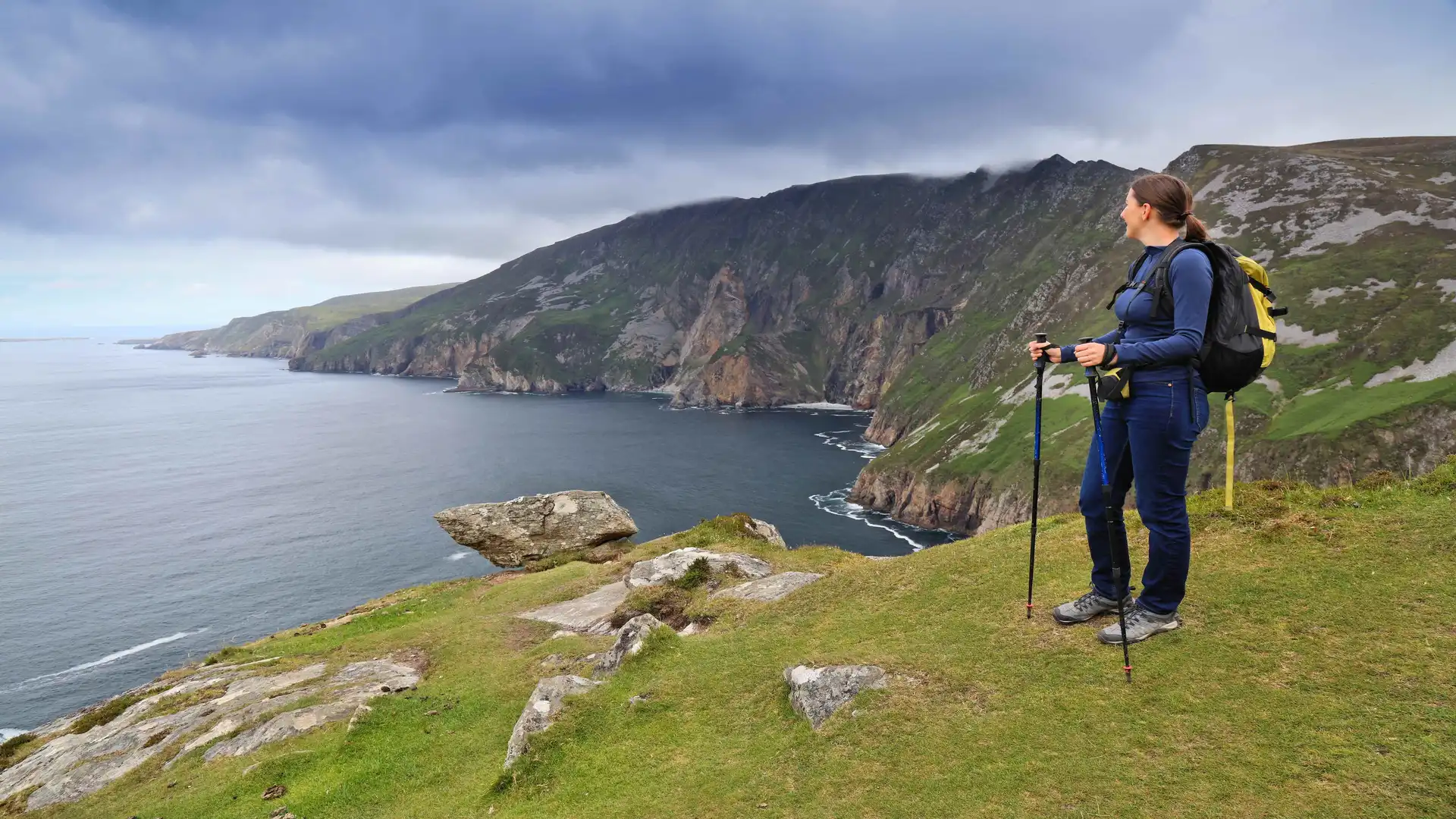 Walker with trekking poles looking out over the dramatic Slieve League Cliffs on the Wild Atlantic Way, County Donegal, Ireland.
