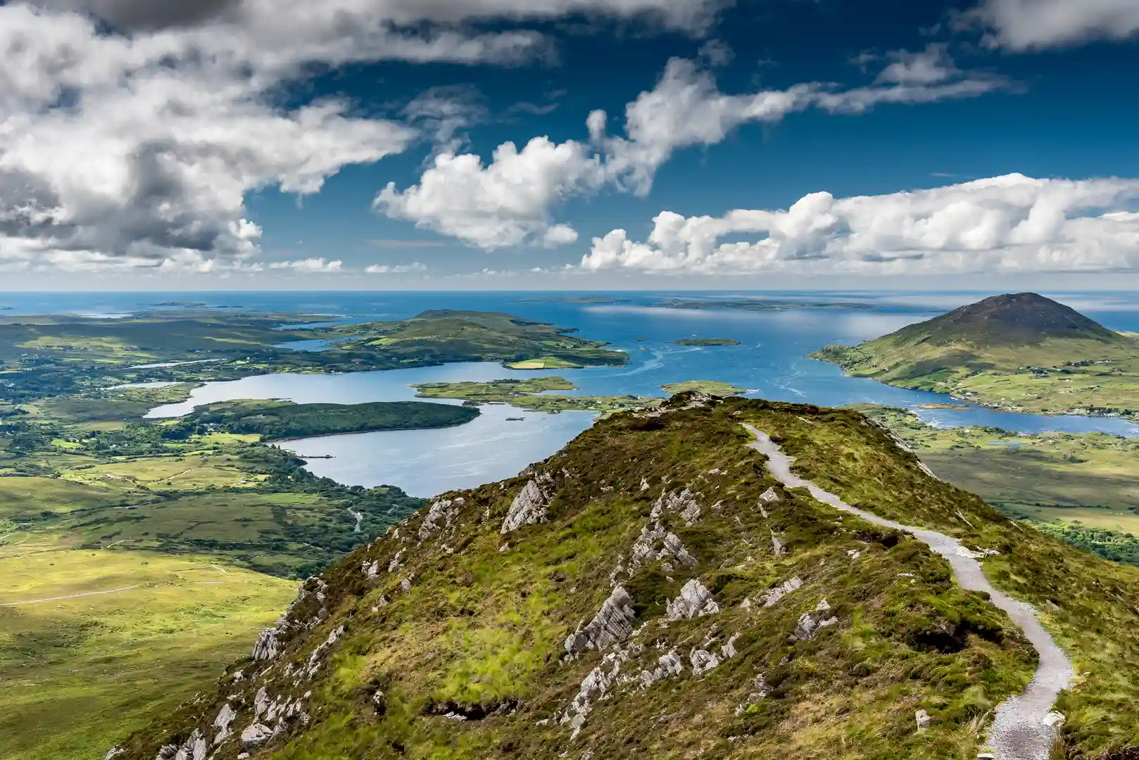 Panoramic view from Diamond Hill in Connemara National Park, County Galway, overlooking mountains, lakes, and the Atlantic coastline under a dramatic sky.