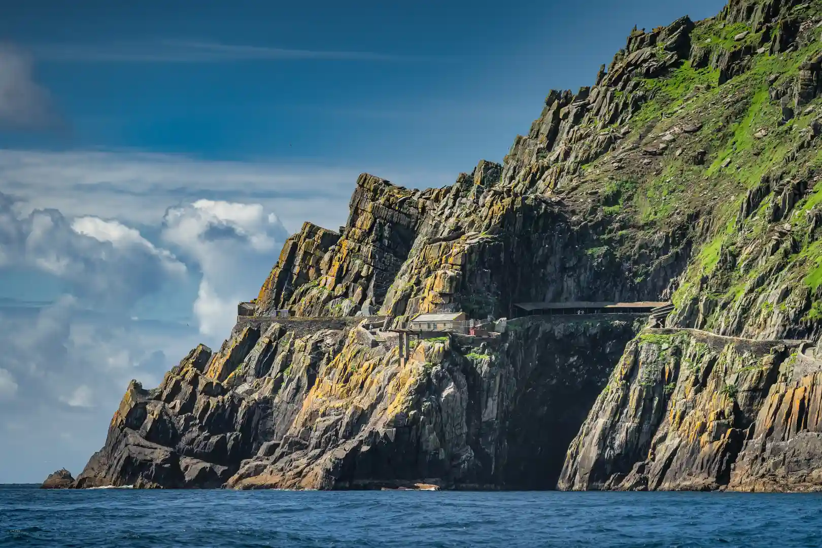 View of Skellig Michael’s rugged cliffs rising from the Atlantic Ocean, with stone steps and landing structures visible at the base of the UNESCO World Heritage Site in County Kerry, Ireland.