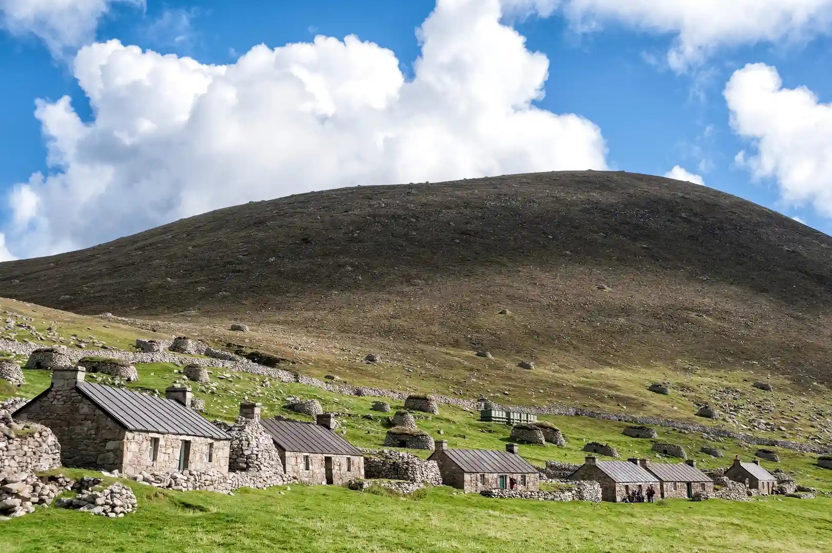 Stone cottages of the abandoned village on St Kilda, Scotland, set against a grassy hillside and wide Atlantic sky in the remote Outer Hebrides.