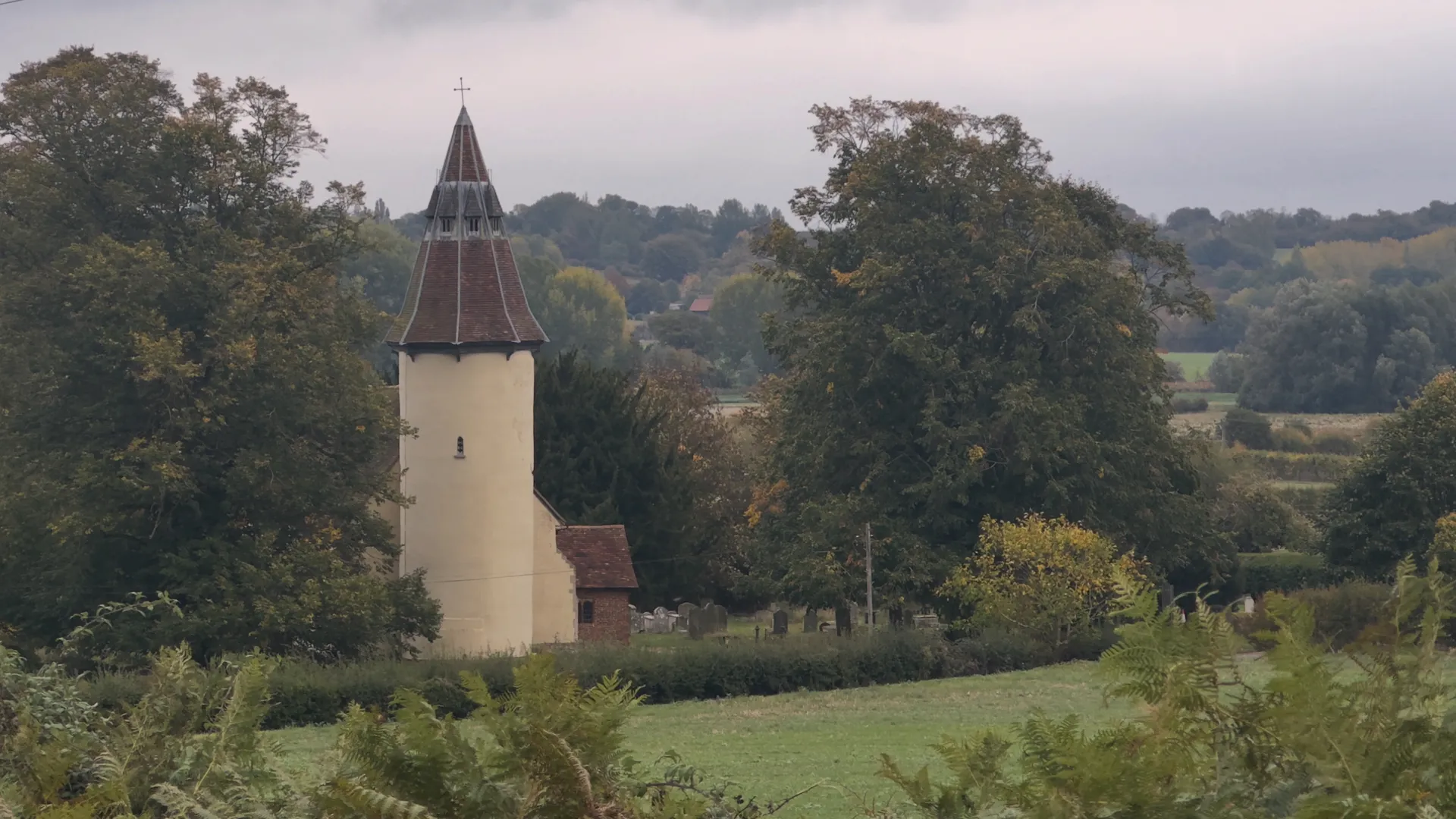 Holy Innocents Church at Lamarsh, a round-tower church overlooking the Stour Valley Path in Suffolk, surrounded by trees and meadows within the Dedham Vale National Landscape.