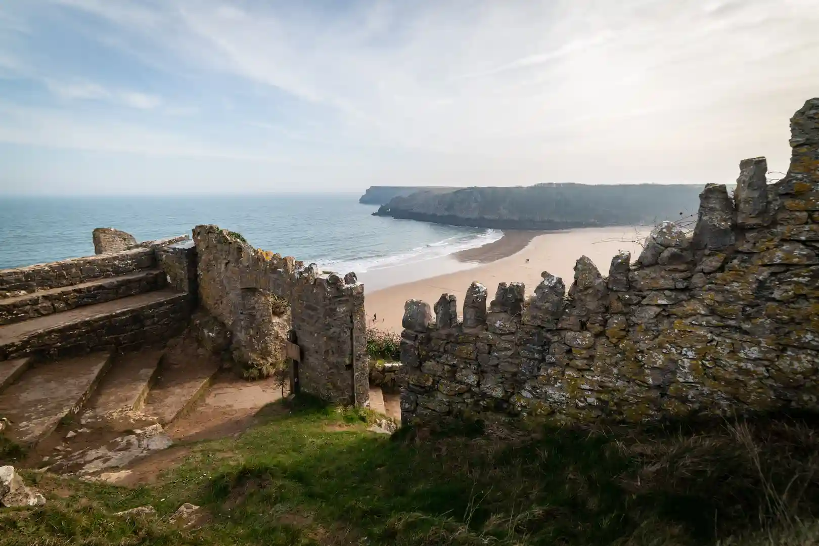 View through ancient stone walls overlooking Barafundle Bay on the Pembrokeshire Coast Path, showing golden sand, cliffs, and sea on a calm day in West Wales.