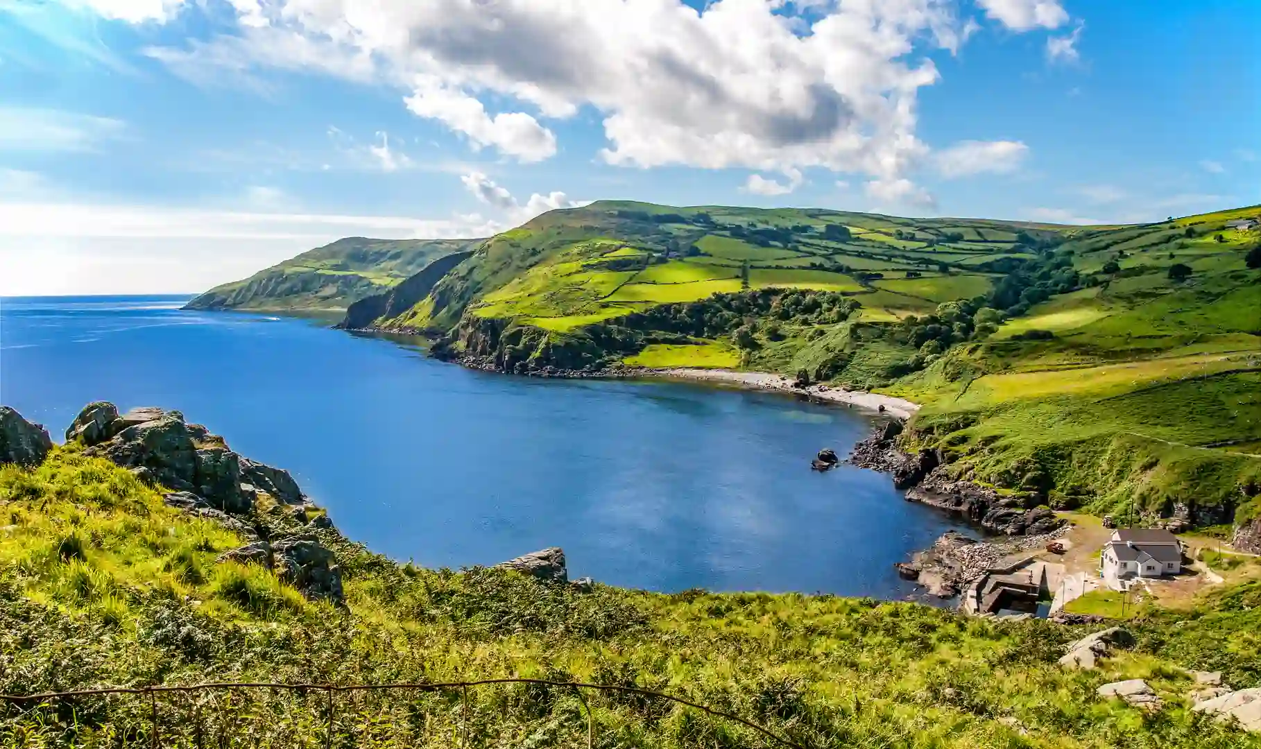 Scenic view along the Causeway Coast in County Antrim, Northern Ireland, showing green hills, cliffs, and blue sea on a sunny day — part of the Glens of Antrim walking area.