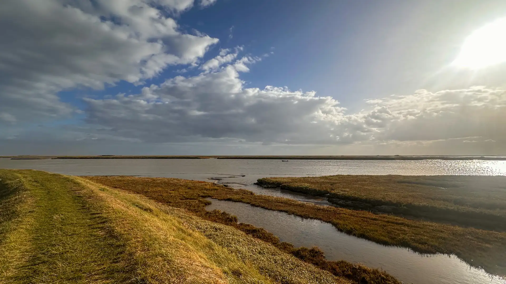 A tidal estuary on the Suffolk coast under bright afternoon light, with grassy sea walls and wide skies — part of the East of England’s network of protected landscapes strengthened under new UK legislation.