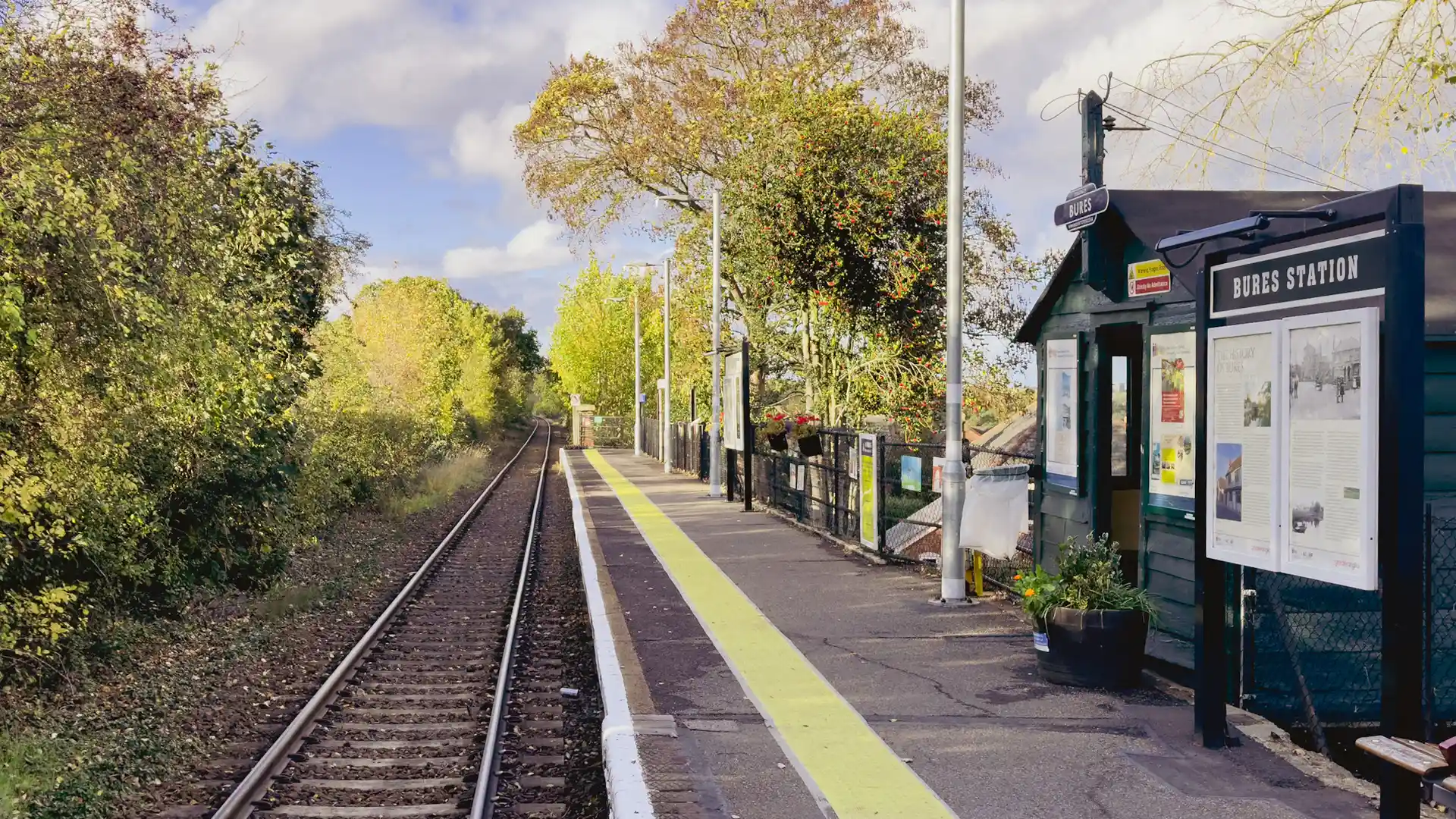 Bures railway station on the Gainsborough Line, with a single rural platform, wooden station building, and tracks leading through trees in the Dedham Vale countryside.