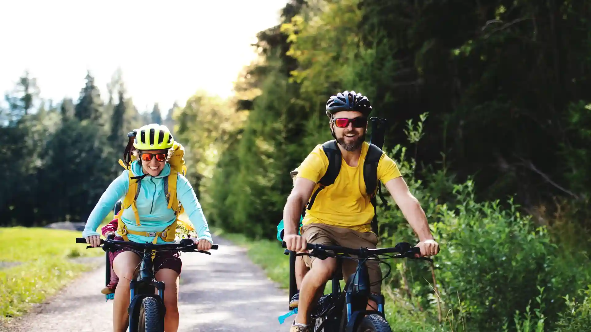 Cyclists enjoying a self-guided cycling holiday along a quiet countryside trail in Suffolk, surrounded by green woodland and summer light.