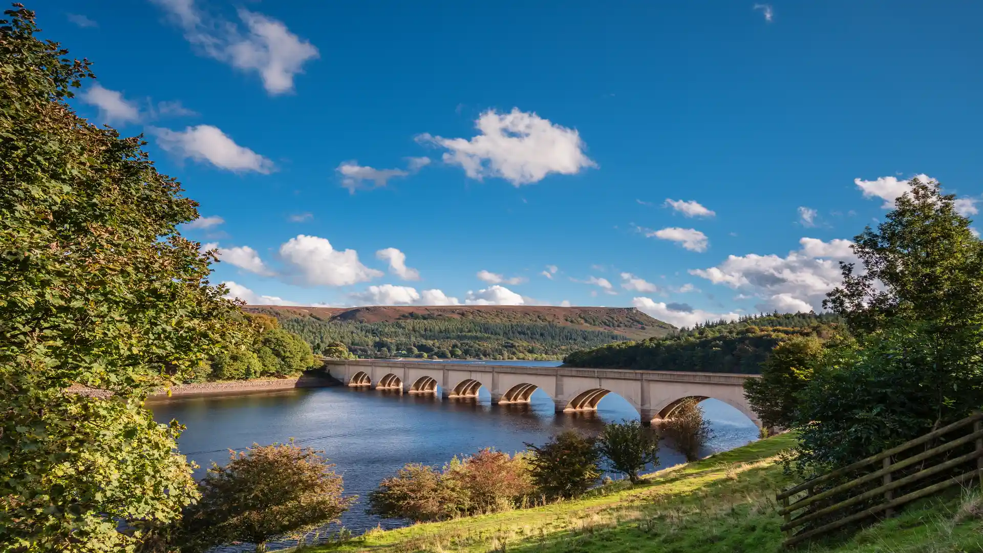 View of Ashopton Viaduct crossing Ladybower Reservoir, surrounded by woodland and moorland hills in the Peak District National Park, England.