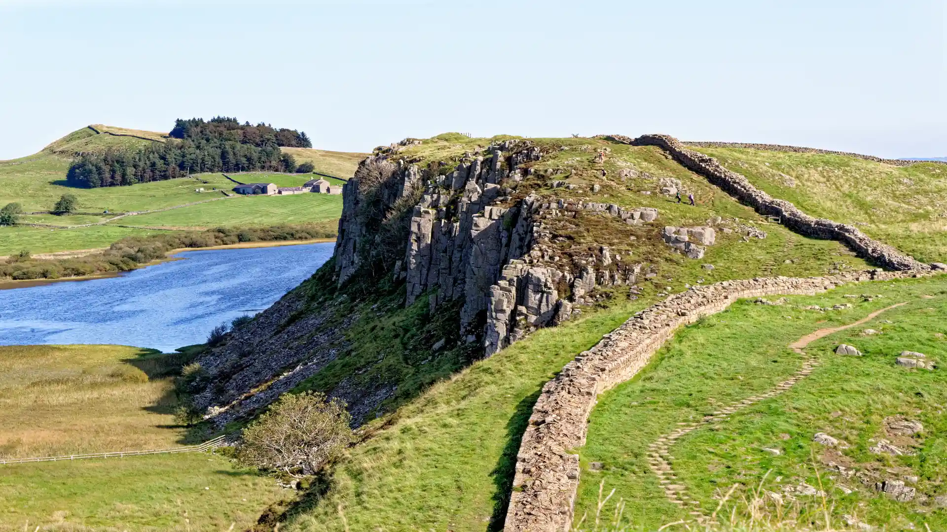 Hadrian’s Wall running along the Whin Sill above Crag Lough in Northumberland, with walkers on the ridgeline of the UNESCO World Heritage Site.