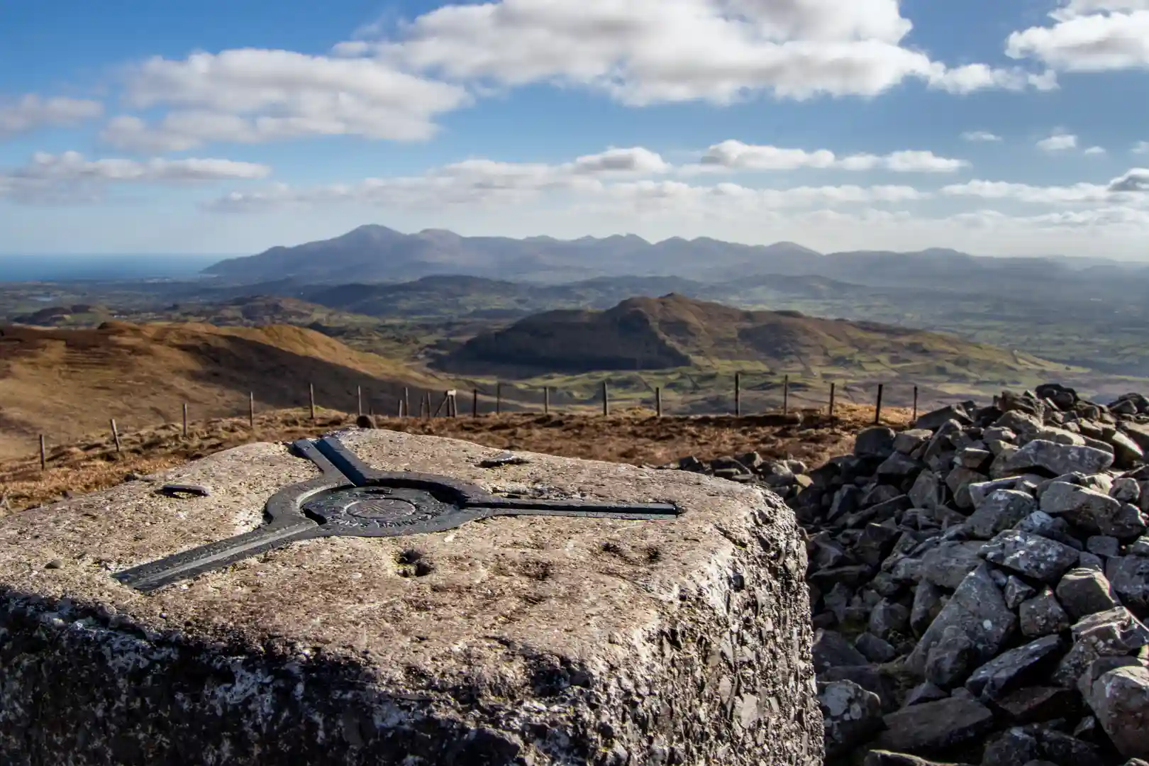 Summit view across the Mourne Mountains in County Down, Northern Ireland, with granite peaks, rolling farmland, and the Irish Sea on the horizon.