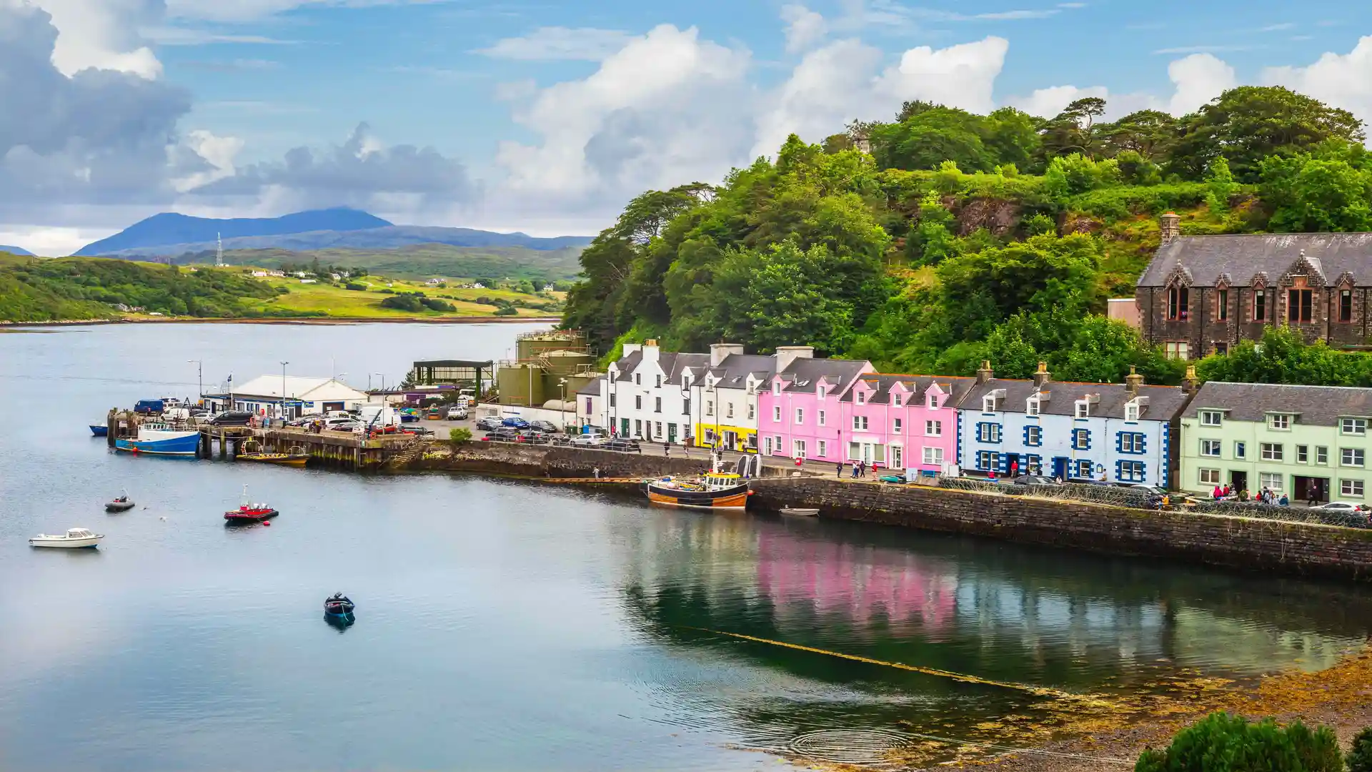 Colourful harbour houses at Portree on the Isle of Skye with boats on calm water and hills in the background, Scottish Islands walking holiday destination.