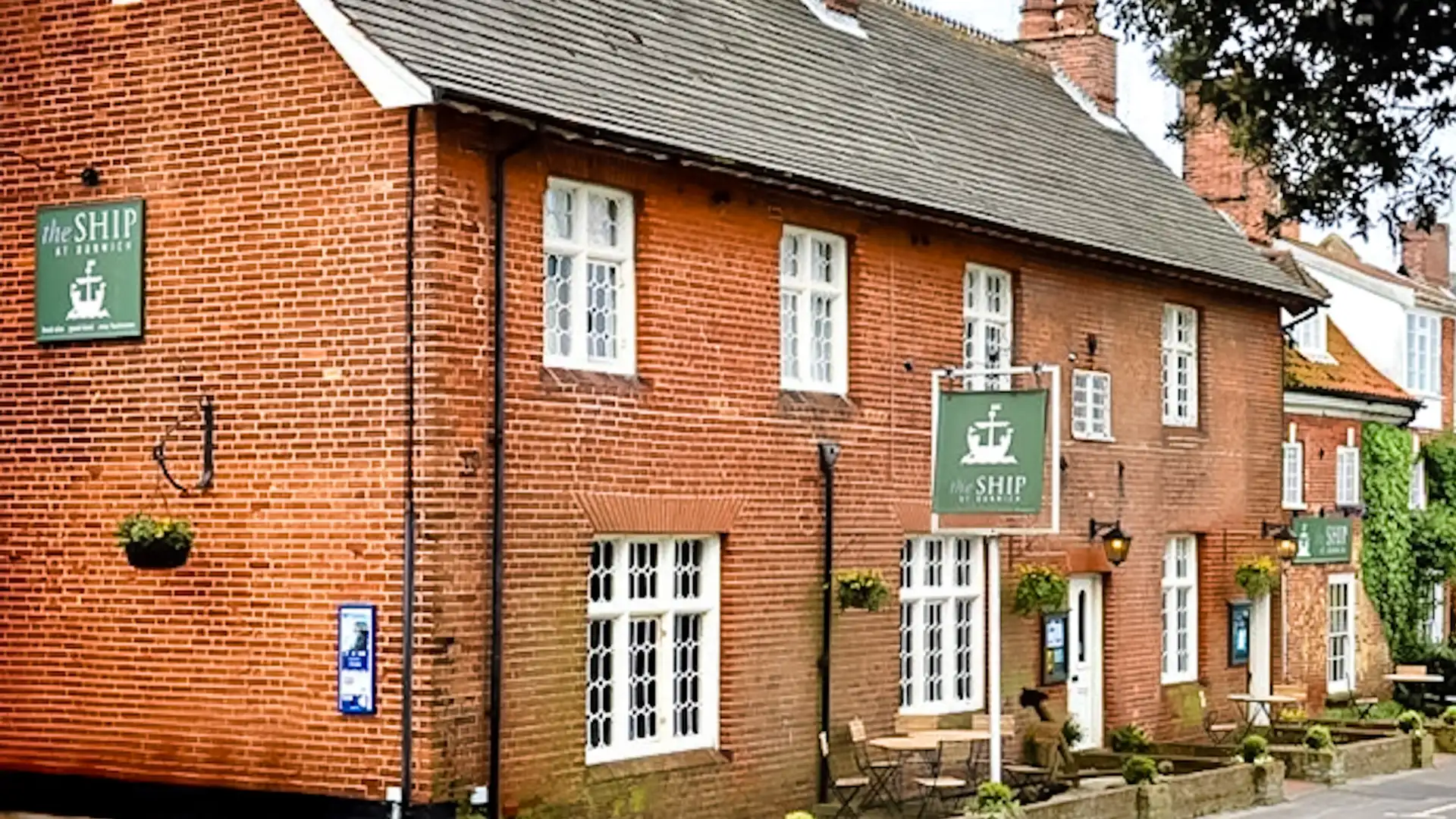 The Ship at Dunwich, a traditional red-brick coastal inn with white-framed windows and hanging pub signs on the Suffolk Coast Path.
