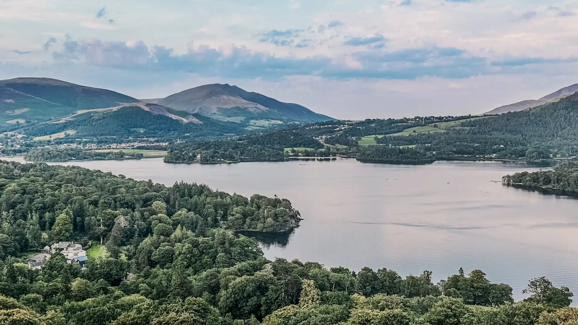 View across Derwentwater in the Lake District UNESCO World Heritage Site with forested shoreline and fells rising toward Skiddaw, a classic walking holiday landscape in Cumbria.