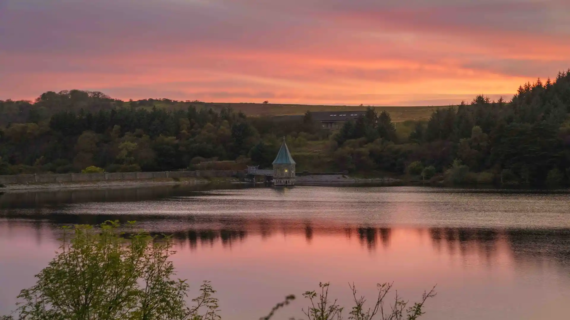 Valve Tower at Pontsticill Reservoir near Merthyr Tydfil, South Wales Valleys, with forested hills and sunset sky reflected in still water.