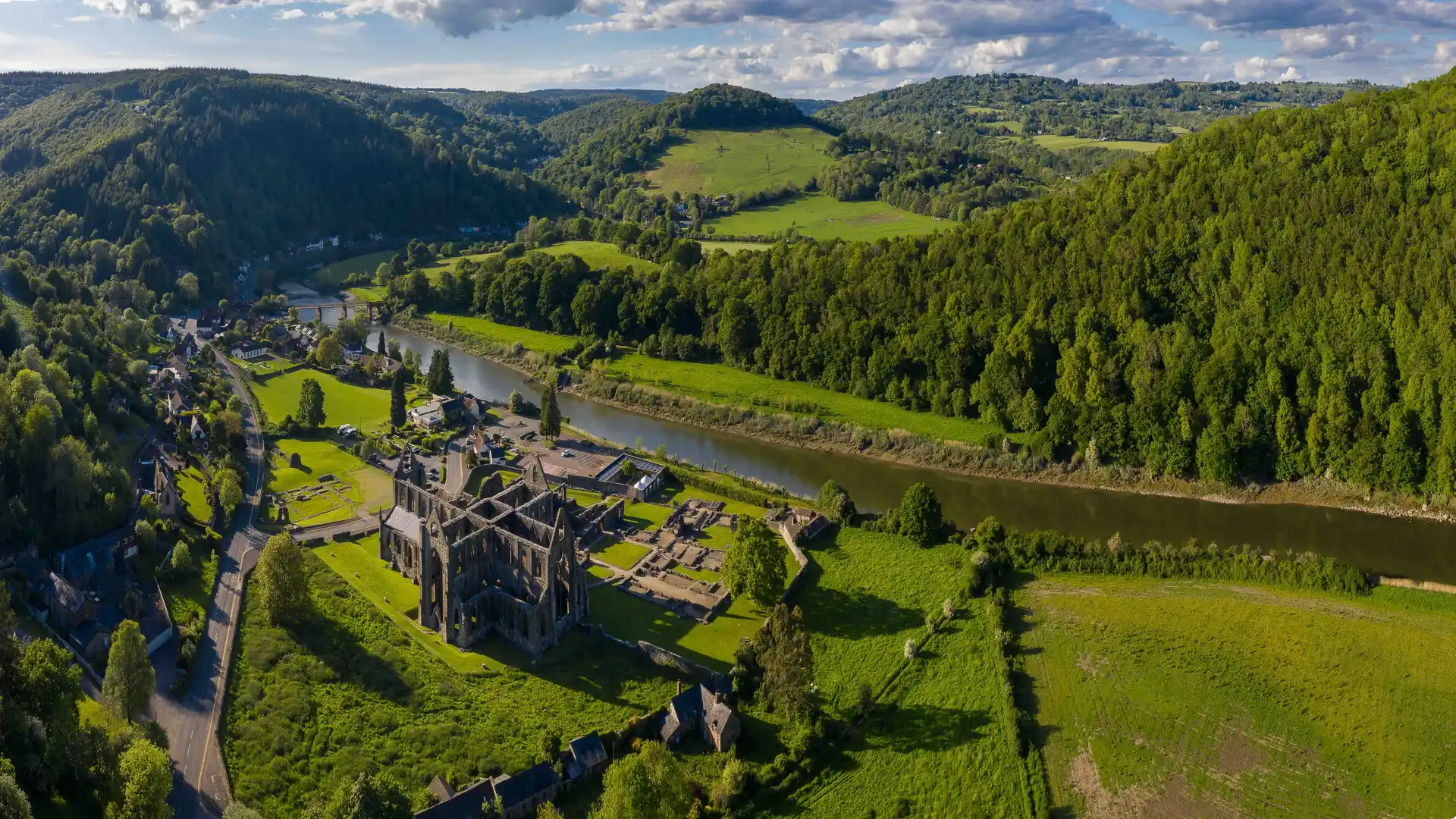 Aerial view of Tintern Abbey in the Wye Valley, with the River Wye winding through green hills and woodlands on the Welsh Borders.