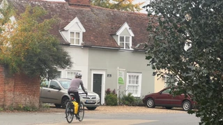 A cyclist rides through a quiet Suffolk village near Dedham Vale, passing traditional cottages and autumn trees — part of the region’s walking and cycling routes.