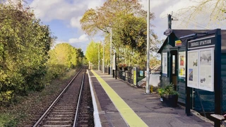 Bures railway station on the Gainsborough Line, with a single rural platform, wooden station building, and tracks leading through trees in the Dedham Vale countryside.