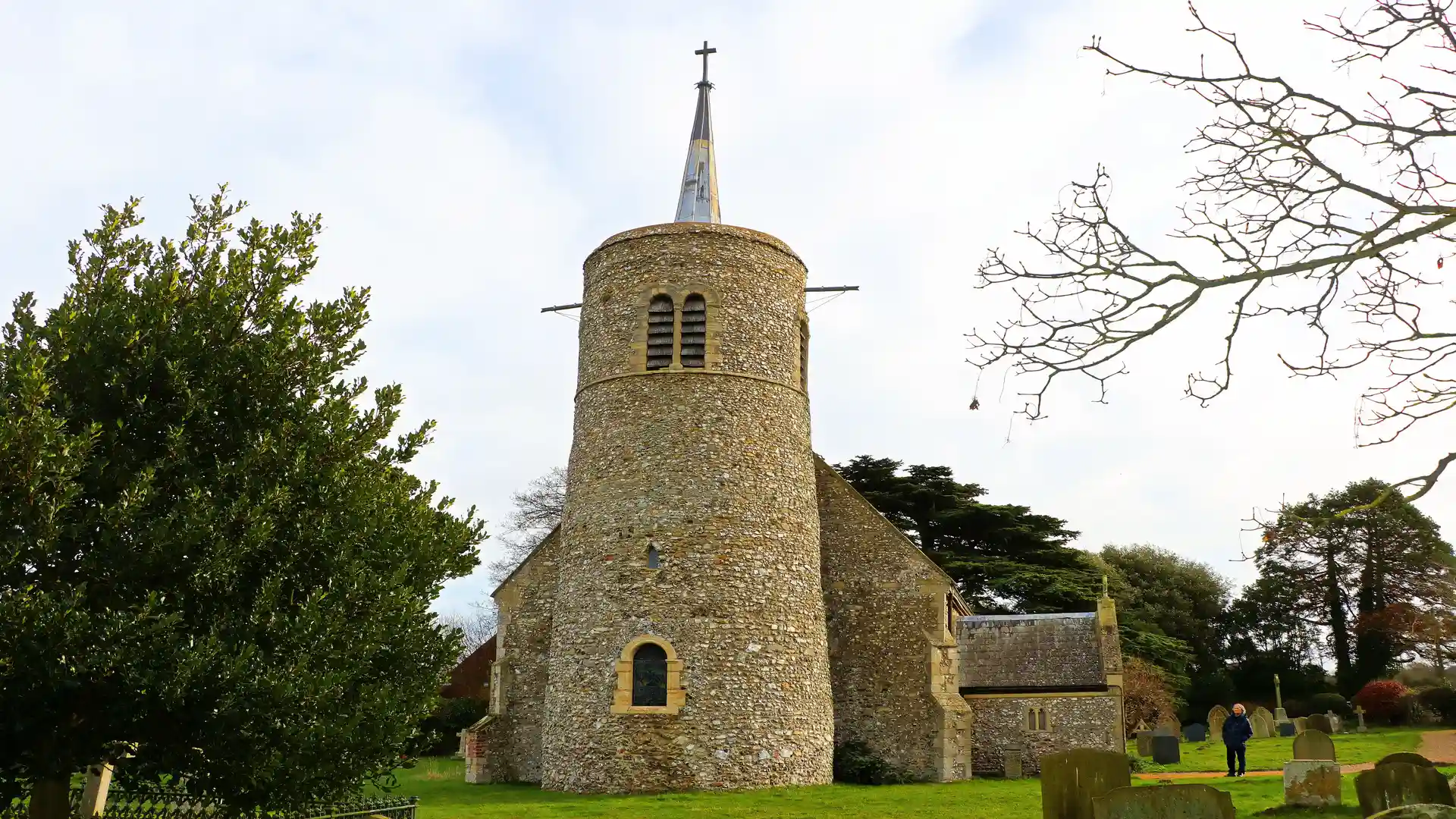 Round tower church in Titchwell, Norfolk, surrounded by grass and gravestones.