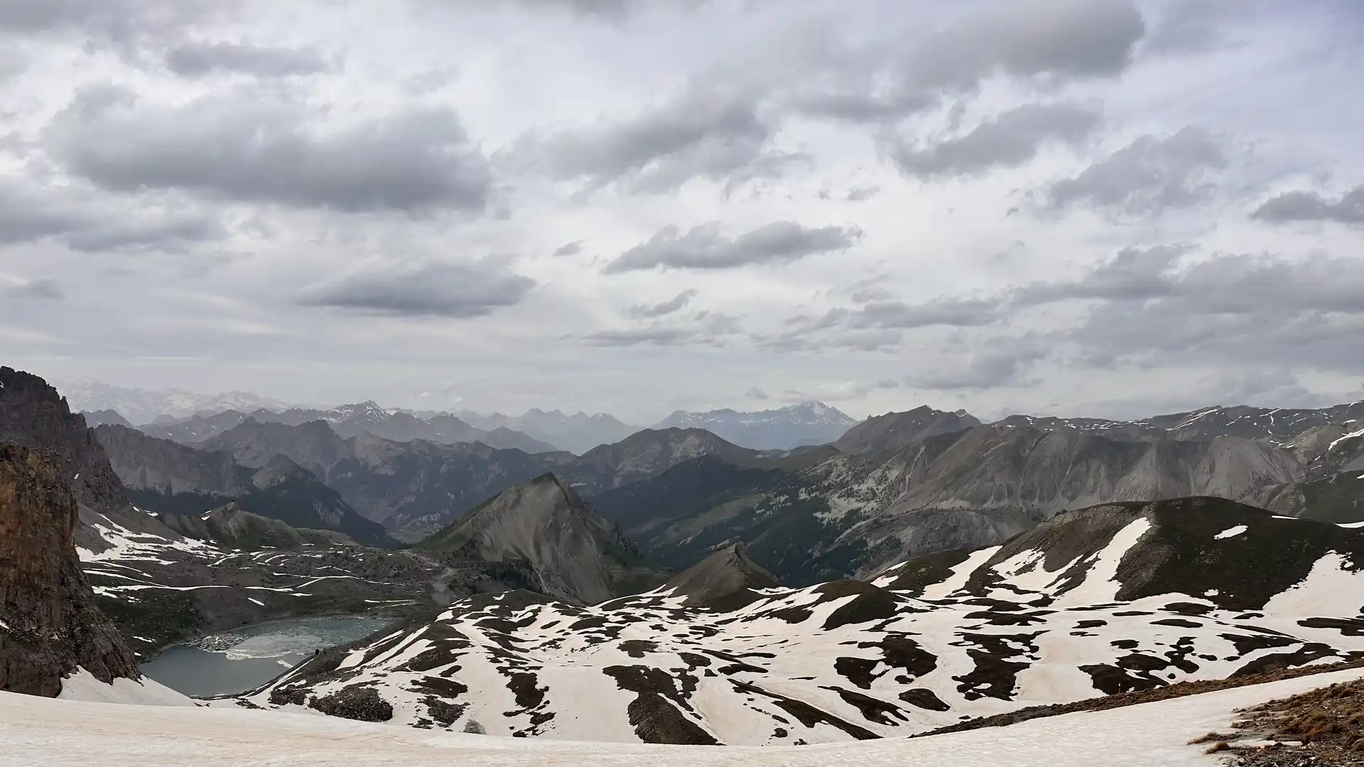 High Alpine landscape in Queyras Regional Natural Park with snow patches, rocky ridges, and a glacial lake below.