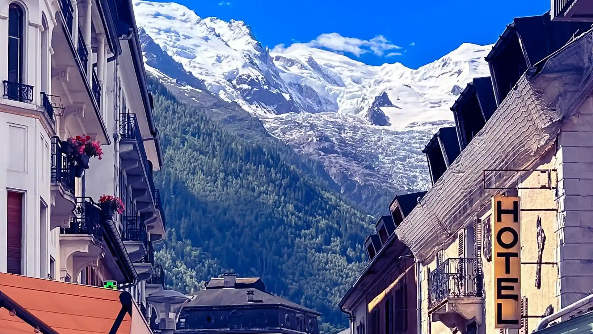 Street view in Chamonix looking toward the Mont Blanc massif, with buildings in the foreground and snow-covered peaks rising above the valley.