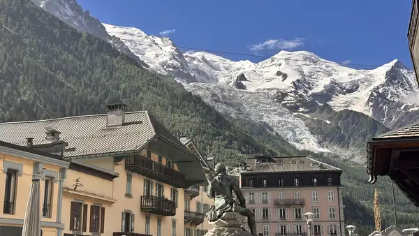 View across Chamonix town toward the Mont Blanc massif, with alpine buildings in the foreground and snow-covered peaks and glacier behind.