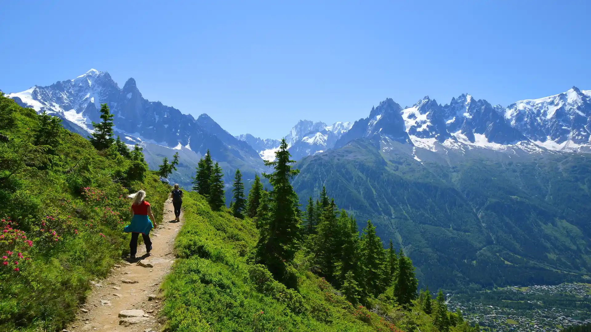 High alpine walking trail with hikers crossing a balcony path above the valley in the French Alps.