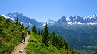 High alpine walking trail with hikers crossing a balcony path above the valley in the French Alps.