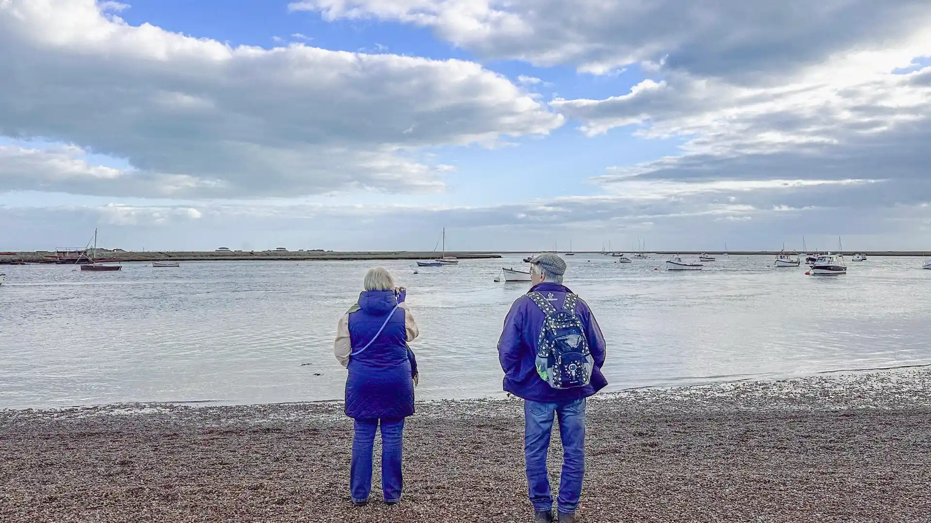 Walkers beside the Orford Estuary on the Suffolk Coast Path, with boats moored on the River Ore.